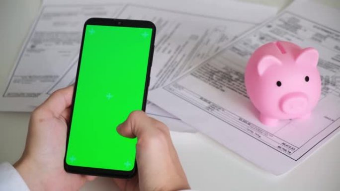 电话与绿屏和存钱罐付款收据，税务文件在白色背景顶视图。智能手机chromakey向不同方向滑动。复制