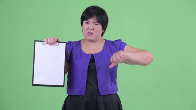 矮胖的亚洲女性肖像，短发拿着白纸，在绿色背景下放下拇指