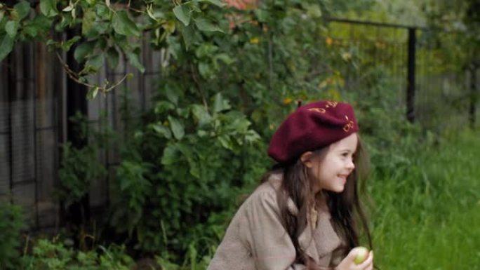 年轻的女孩从水果园的树上摘下成熟的苹果。微笑的少女，穿着贝雷帽和外套，拿着乡下果园里果树上的新鲜苹果