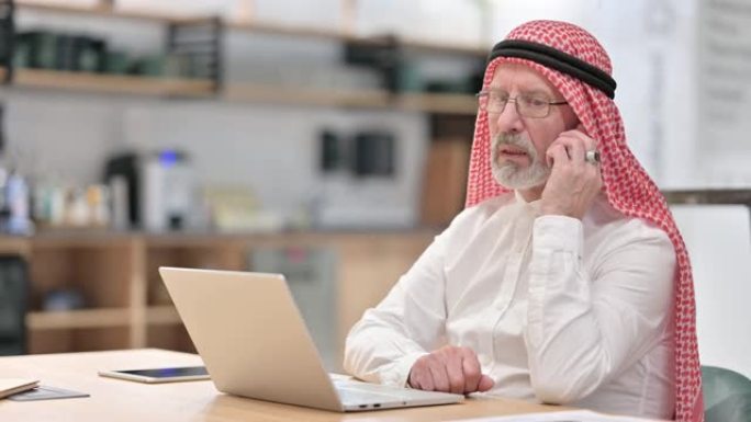 老阿拉伯商人，笔记本电脑在智能手机上聊天