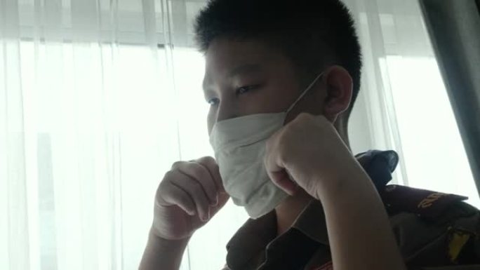 快乐的亚洲童子军在早上上学前戴着口罩在附近的窗户上有太阳光，这是新型冠状病毒肺炎期间的新常态概念。