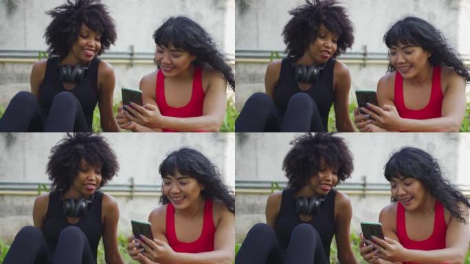 由两个女性健身朋友组成的多元化团体在公园里聊天和使用手机。年轻女性在户外休息和微笑