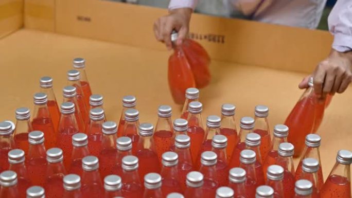 工人从纸板箱中提取瓶装果汁，然后在饮料加工厂包装。