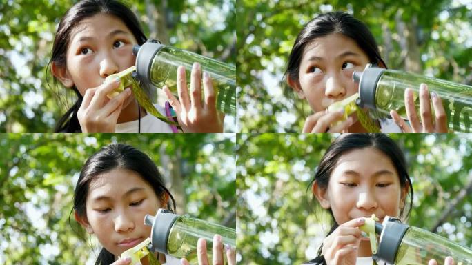 快乐的亚洲女孩在冒险之旅中在森林里喝一瓶水。