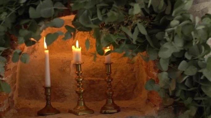 在装饰有树枝的石墙深处的老式烛台上燃烧蜡烛
