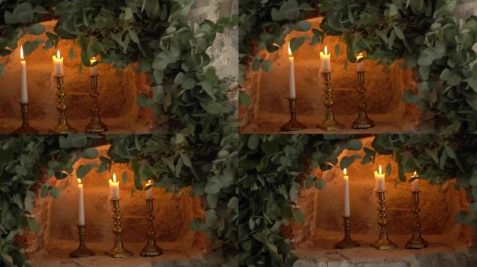 在装饰有树枝的石墙深处的老式烛台上燃烧蜡烛