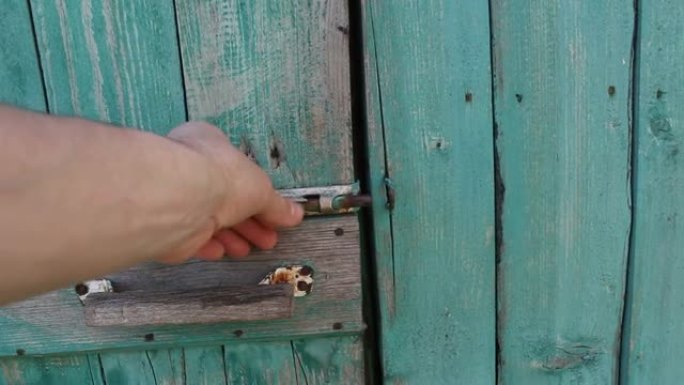 男性手打开旧门的锁。男性手的特写打开一扇涂有油漆的旧门