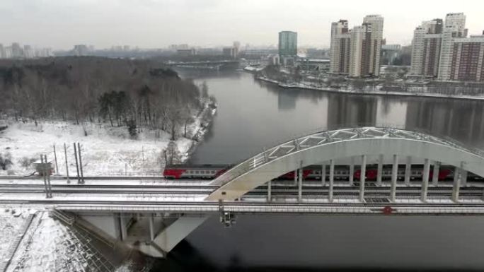 跟踪在冬天的城市背景下，在河上的一座桥上拍摄了高速旅客列车的运动。乘火车旅行。