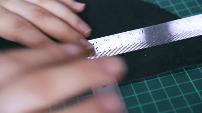 裁缝移动金属尺测量黑色皮革布料