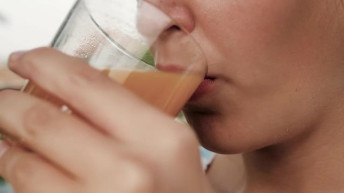 女人正在喝桃汁。女性手的侧视图将装有桃汁的玻璃杯带到嘴里，并在大自然的晴天喝。特写