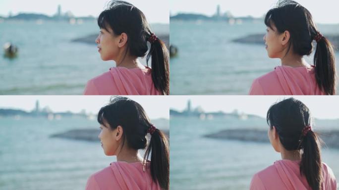 一个年轻的亚洲女子微笑的肖像放松享受宁静的日落，仰望呼吸新鲜空气放松美丽的风景海景。