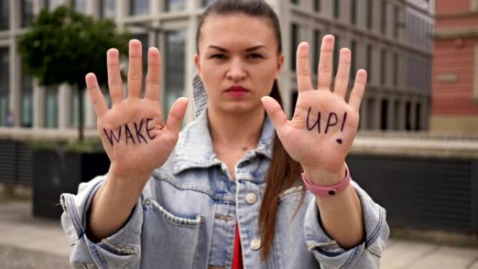 单一的抗议者。一位严肃的年轻女子拿出她的手掌，上面写着“醒醒”。她呼吁采取行动
