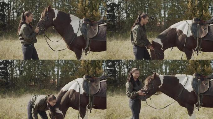 一位年轻漂亮的女骑手在艰难而遥远的骑马徒步旅行后，向她最喜欢的母马抚摸，休息和吃新鲜的草