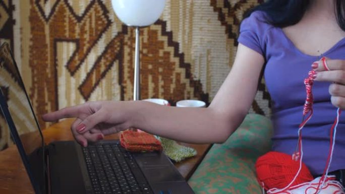 手提电脑屏幕上的特写。迷人的黑发妈妈坐在沙发上的房间里，从互联网视频课程中学习编织。创意家庭休闲呆在