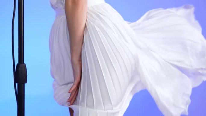梅林·门罗在复古麦克风附近摆姿势的漂亮年轻女子。一件白色短裙在风中飘扬。金发女郎在浅蓝色工作室背景下
