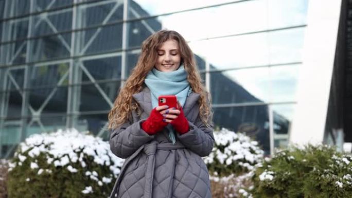 女人在智能手机上发短信，站在冬天的城市的街道上新年。女性在户外窃听手机。现代假期网上购物，购买新年礼