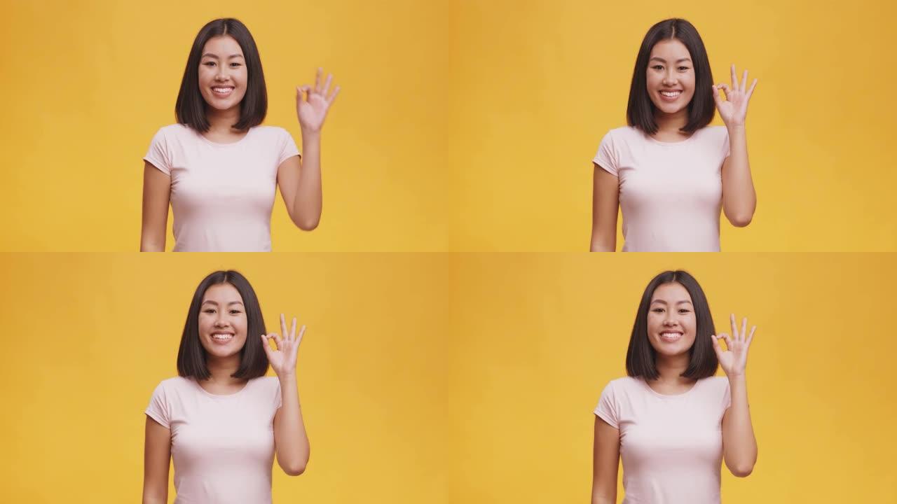 一切都很好。积极的年轻亚洲妇女打手势，对相机微笑，橙色背景