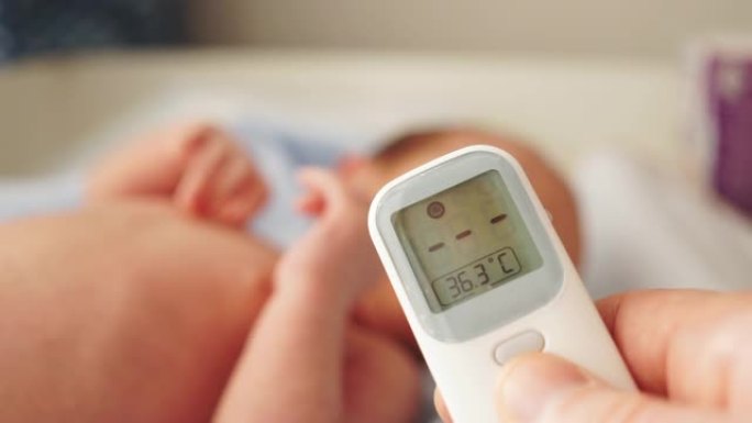 母亲或父亲用数字非接触式温度计测量婴儿温度。这个孩子几个月大。婴儿体温正常。