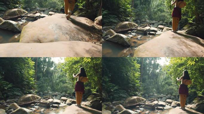 亚洲女性旅行者在热带森林中，有水流和落水的背景。自然旅行的概念。4k慢动作。