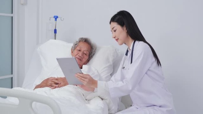 亚洲女医生拿着数字平板电脑给病人看，老病人女人躺在床上。