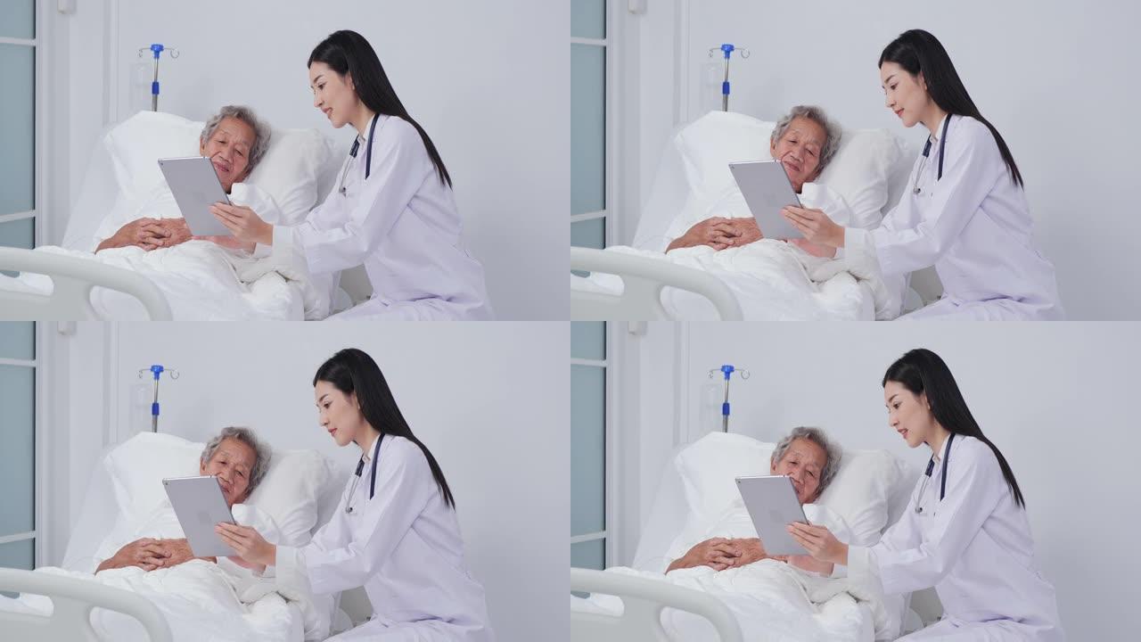 亚洲女医生拿着数字平板电脑给病人看，老病人女人躺在床上。