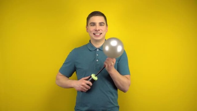 一个年轻人用黄色背景上的泵给一个银色气球充气。穿着绿色马球的男人。