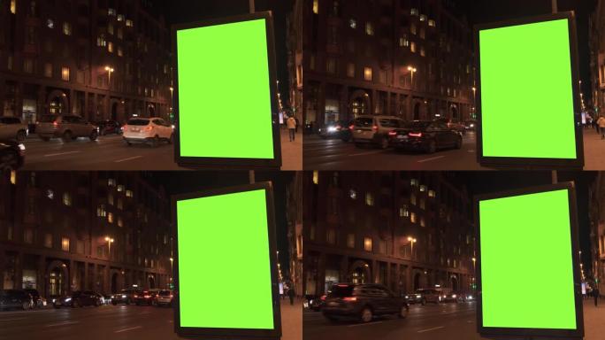 带有绿色屏幕的广告牌，位于繁忙的街道上。汽车在晚上行驶。