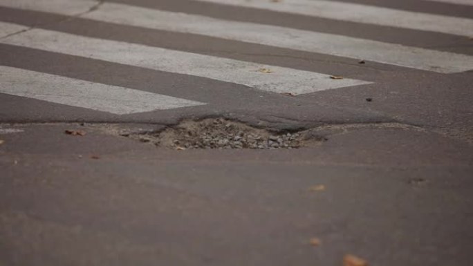 城市道路上的坑洼。断路。人行横道。汽车车轮。特写