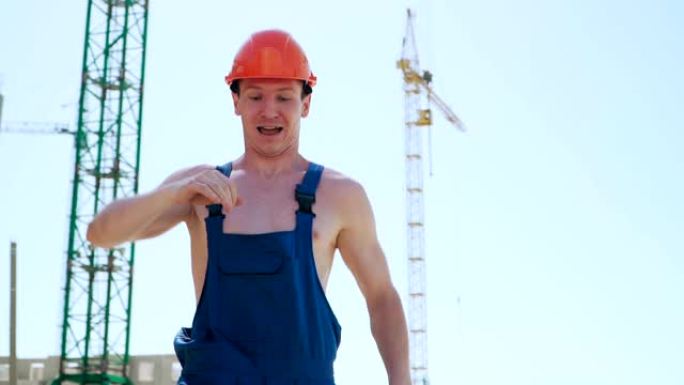 戴着安全帽跳舞的快乐高加索人建设者。工人在建筑工地的背景下滑稽动作。慢动作。斯蒂安卡姆射击。