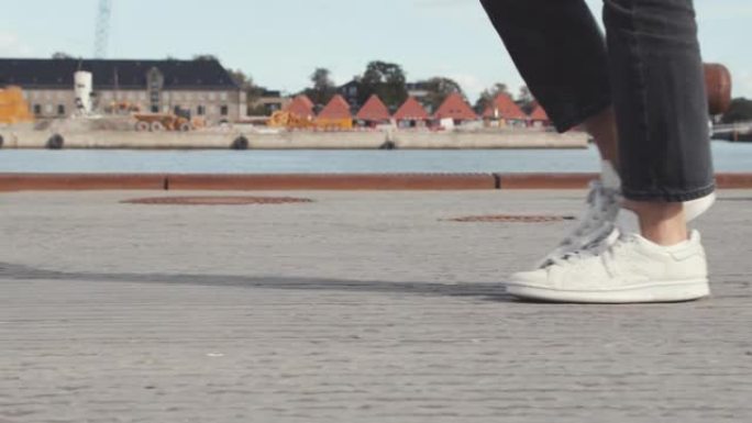 一对穿着白鞋的女人的腿在哥本哈根码头的码头上行走