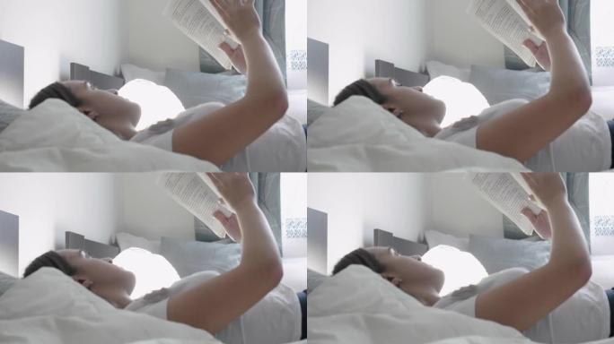 甜蜜的家。新常态。年轻的千禧一代妇女躺在床上读一本模拟书。新型冠状病毒肺炎期间呆在家里。在家中的简单