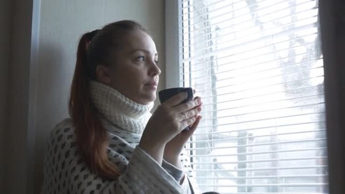 在冬天的日子里，生活方式的女人坐在窗边，端着一杯热茶