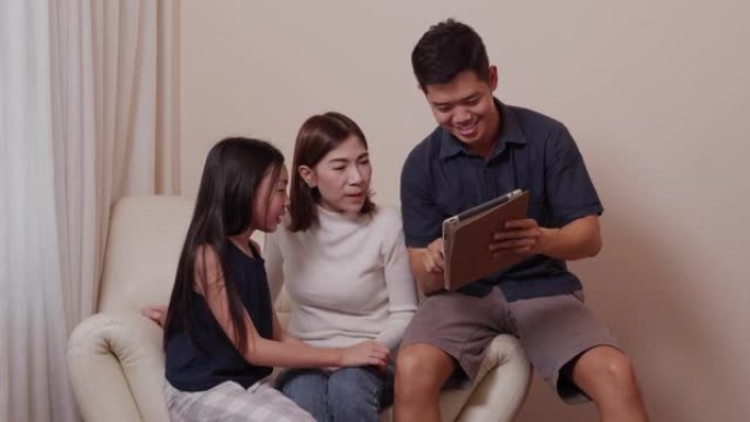 亚洲幸福的父母和漂亮的女儿在家庭时间一起在客厅使用平板电脑上的小工具时很享受。