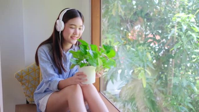 可爱的亚洲年轻女子喜欢看花盆里的绿色植物，她坐在玻璃窗前