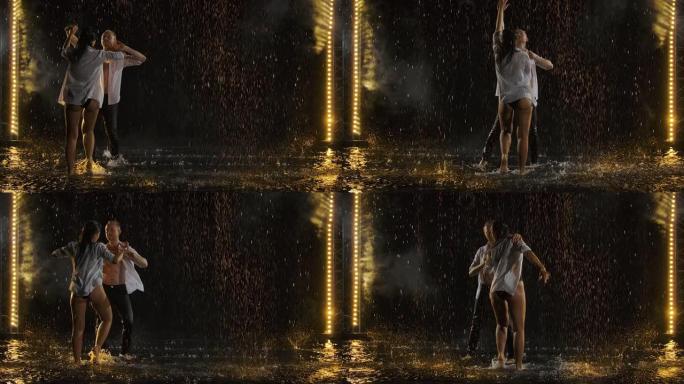 激情的湿情侣在雨中亲吻和跳舞。雨点间的爱情故事。以慢动作拍摄在烟熏黑的工作室背景与舞台灯光