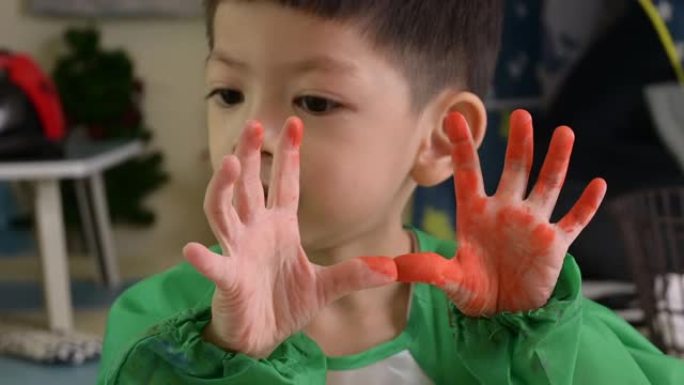 快乐的孩子用橙色水彩展示肮脏的手
