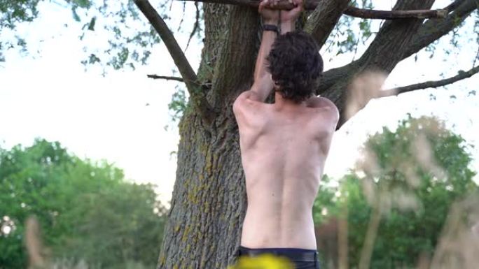 光着膀子的肌肉男人在公园的树上做拉起运动的后视图。高质量4k镜头