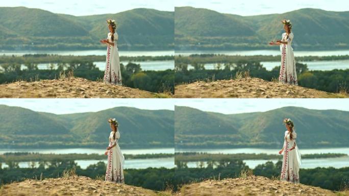 美丽的年轻女子站在小山上，头上戴着花环，穿着带有刺绣的民间服装。女人用手唱民歌和手势，大自然的广阔。
