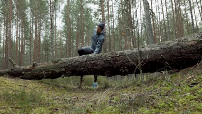 男子在森林小径上奔跑，跳过倒下的老树。慢动作滑块拍摄
