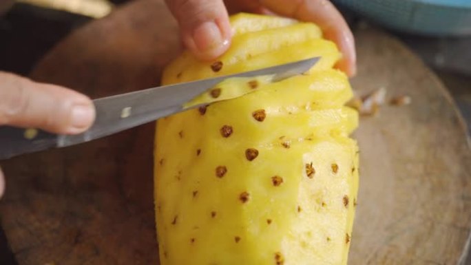 菠萝被一把小刀从里面剥去不好的部分。亚洲老太太家庭主妇。自然照明的宏观拍摄。