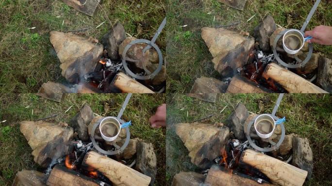 篝火和咖啡的特写。年轻人坐在篝火前，在秋天露营时加热咖啡。
