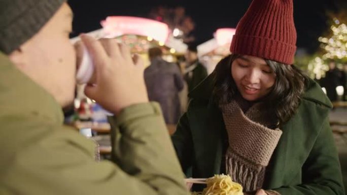 亚洲夫妇穿着暖和的衣服在圣诞节吃街头食物。