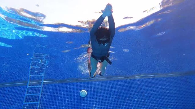 水下底视图倾斜女人穿一件长袖比基尼剪裁潜水服做动态呼吸暂停游泳finning颤振踢与双鳍在游泳池