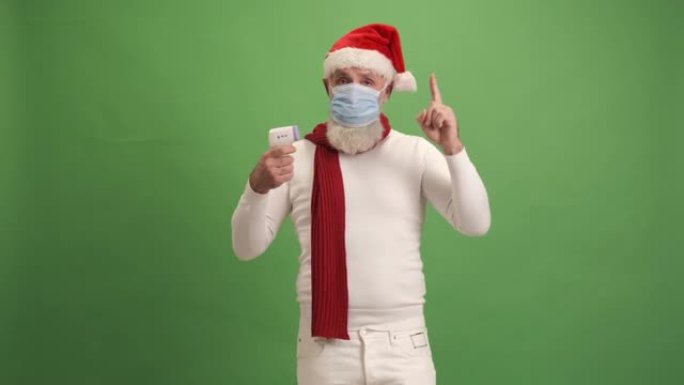 戴着医用口罩的老人显示数字温度计，并在绿色背景上显示抬起的手指。一个人。