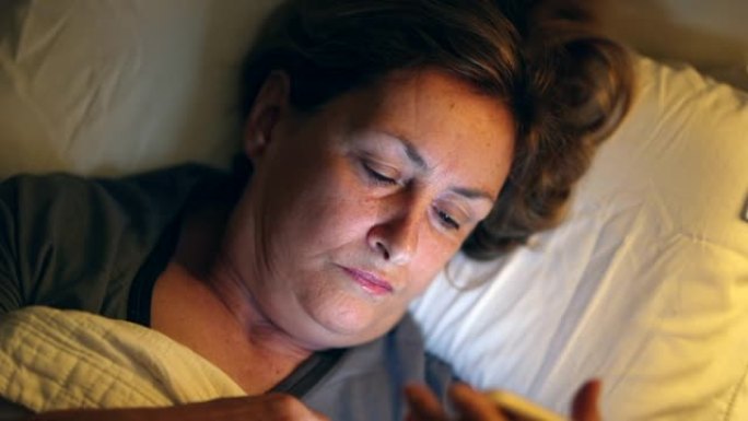 躺在床上的老妇人看着盯着蓝光屏幕的手机设备