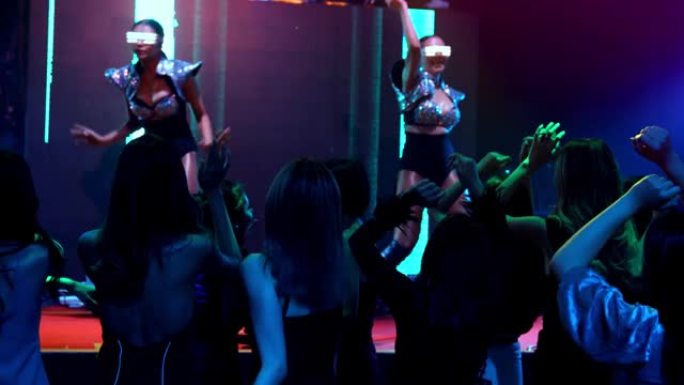一群人在迪斯科夜总会里随着舞台上DJ的音乐节拍跳舞