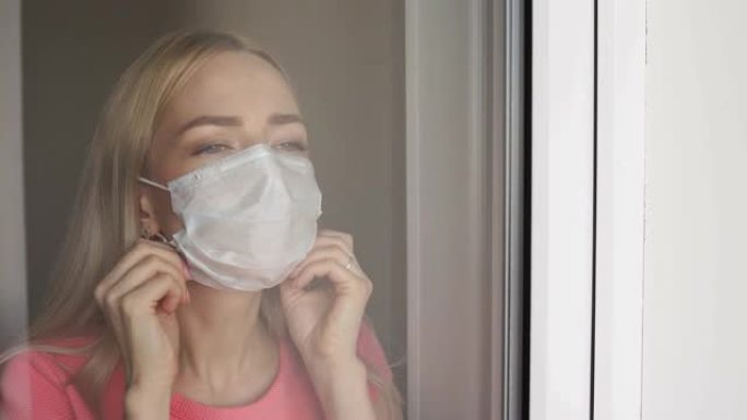 家庭检疫。白人妇女戴着医用口罩站在窗前，向外看