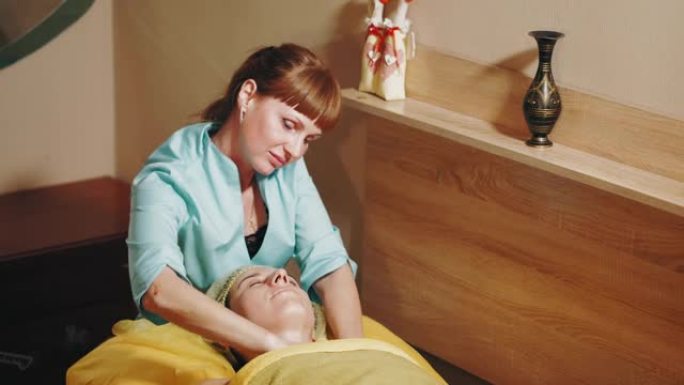 抗衰老美容。面部按摩。女人正在美容诊所接受面部和肩部按摩，以调理肌肉和面部皮肤淋巴引流。皮肤护理，女