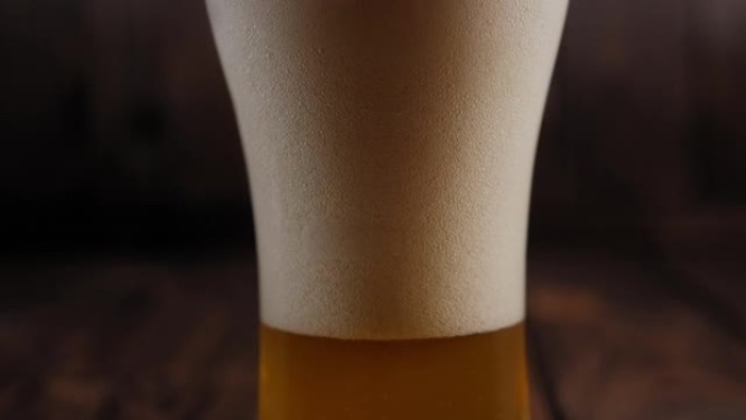 一杯淡啤酒，木质背景上有很多泡沫和气泡。