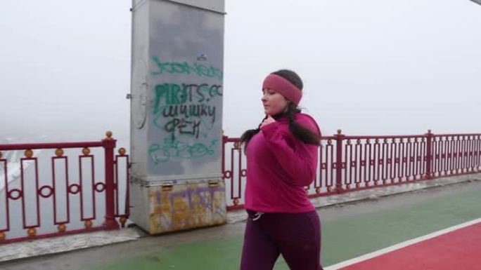 年轻胖乎乎的高加索女孩在桥上奔跑。侧射慢动作。紫色套装